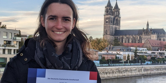 Eine Frau steht vor einer Skyline und hält eine Urkunde in den Händen