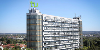 Mathematikgebäude mit Mathetower Mathematikgebäude mit Mathetower: Ein hohes Gebäude mit vielen Fenstern und je einem Turm an beiden Seiten. Auf dem linken Turm ein grünes TU-Logo. Im Hintergrund Häuser und Bäume.